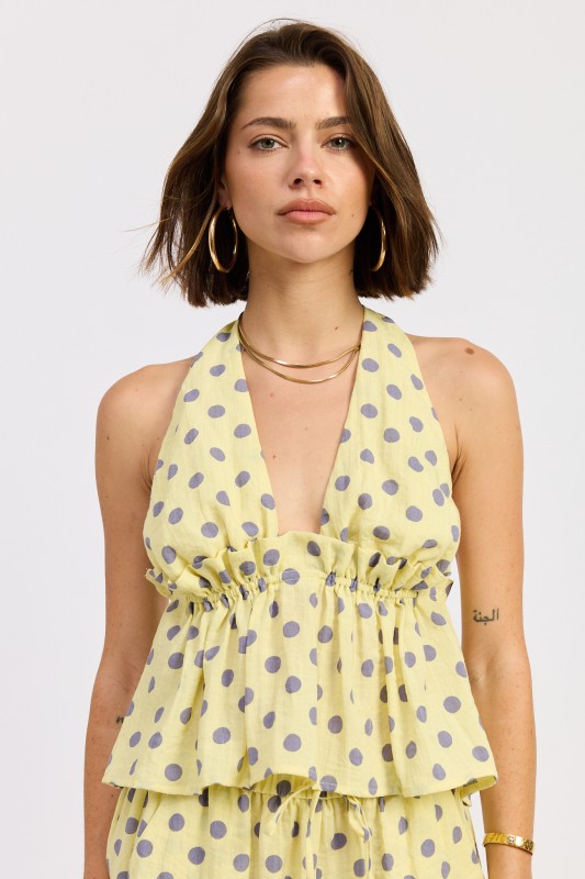 Woman wearing a butter yellow polka dot halter top with ruffle detail and flowy fit