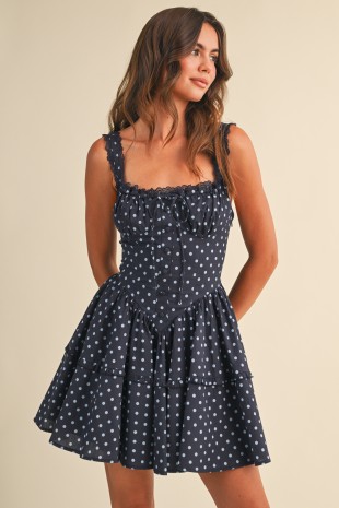 Woman wearing a navy polka dot corset mini dress with lace trim and tiered skirt