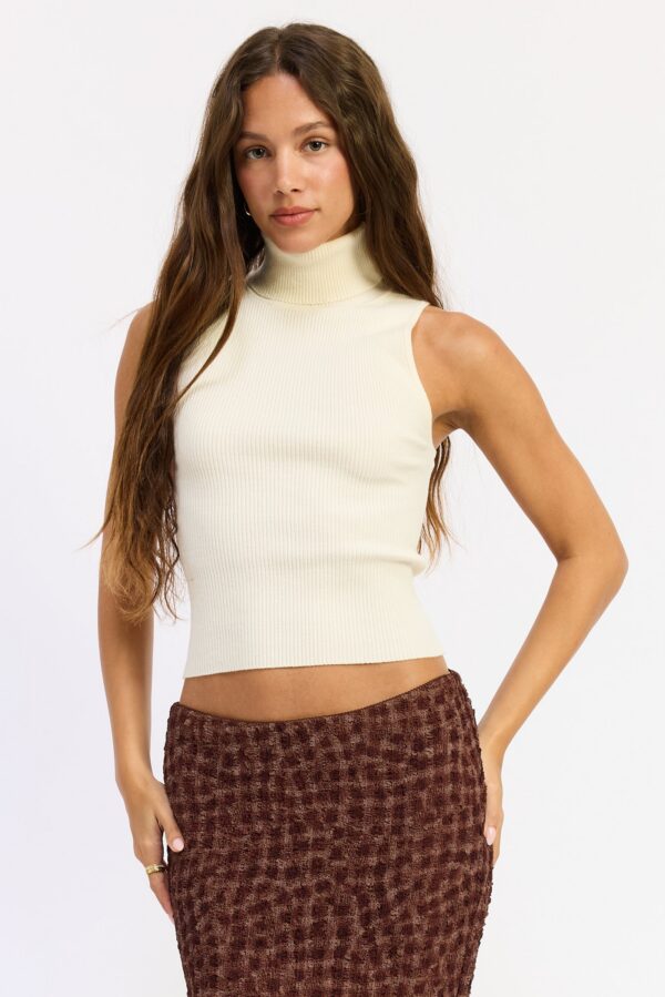 Ivory top featuring a sleeveless cut, polished turtleneck, smooth sweater knit, and close streamlined silhouette