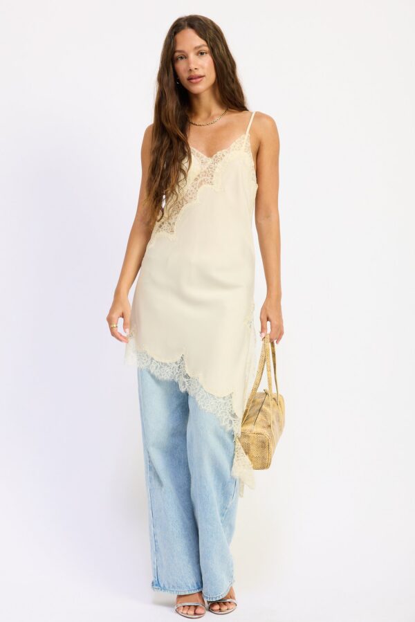 Cream top with spaghetti straps, a satin finish, lace detail, and an asymmetrical longline silhouette styled for a women’s boutique fashion look